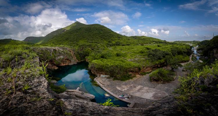 A lush green mountainous landscape with a water body.