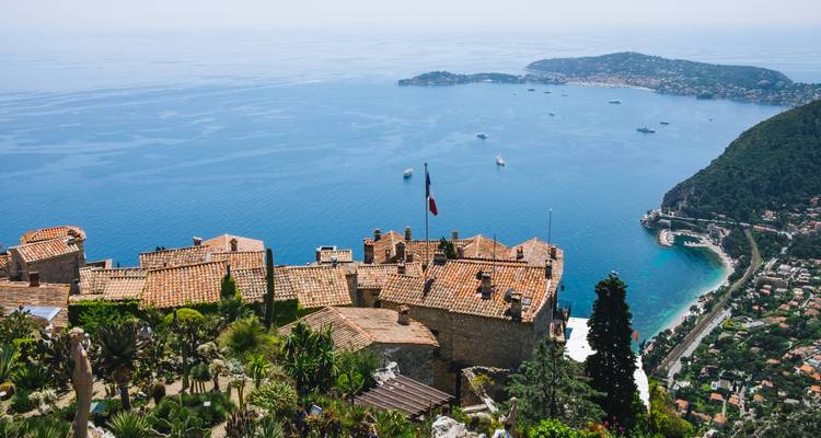 Vue panoramique d'une ville côtière avec des toits en terre cuite et un drapeau.