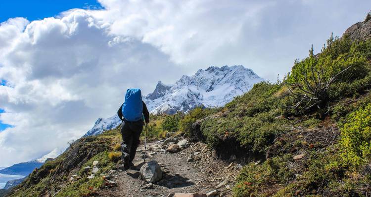 Hiker with backpack approaching snowy mountains.