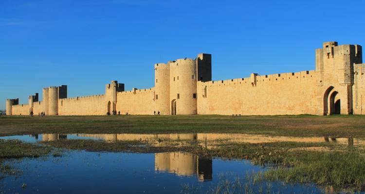 Murs historiques se reflétant dans un plan d'eau sous un ciel bleu.