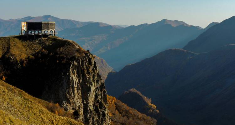 Stenen monument op een klif met uitzicht op ruige bergen.
