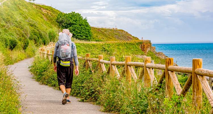 A person walking on a coastal path with a backpack.