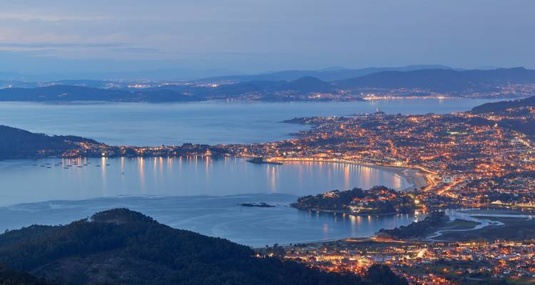 Vue nocturne d'une ville côtière avec front de mer illuminé.