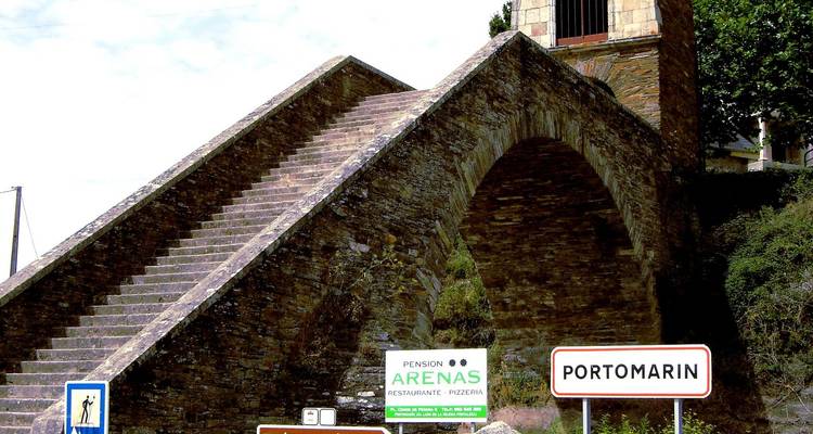 Historic stone bridge with a sign indicating Portomarin.