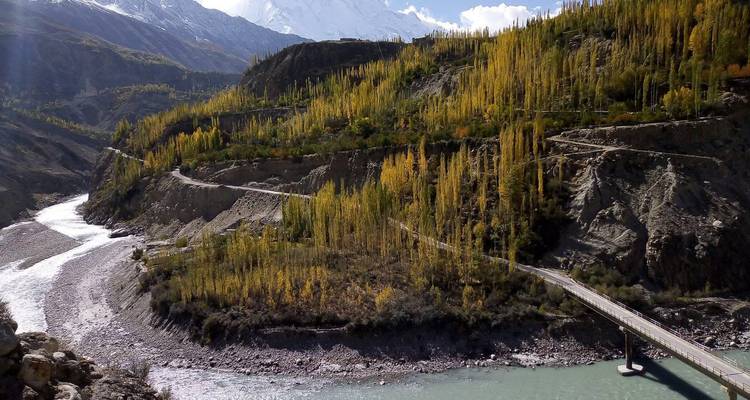 Slingerende weg en turquoise rivier meanderen door een diepe vallei omlijst door gouden populieren en met sneeuw bedekte toppen