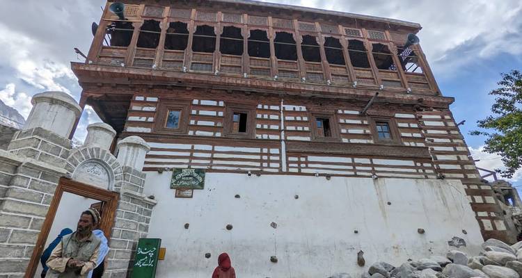 Palais traditionnel en bois et pierre avec balcons en bois rayés se détachant contre un ciel partiellement nuageux