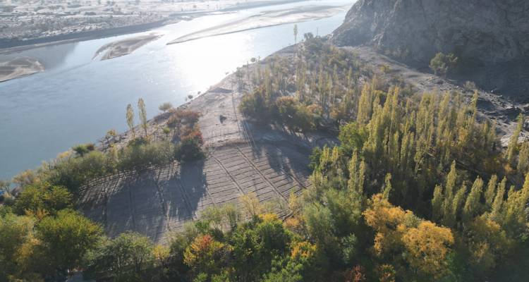 Vue aérienne d'un large méandre de rivière, terrain en terrasses et arbres d'automne colorés avec des montagnes rocheuses en arrière-plan.