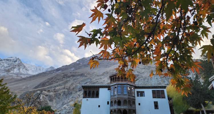 Palais blanc historique encadré par des feuilles d'automne colorées avec des montagnes dénudées qui s'élèvent derrière.