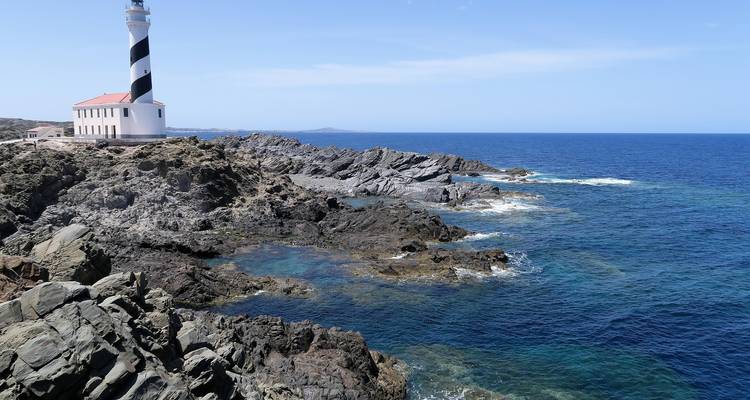 Phare rayé sur une côte rocheuse avec mer bleue.