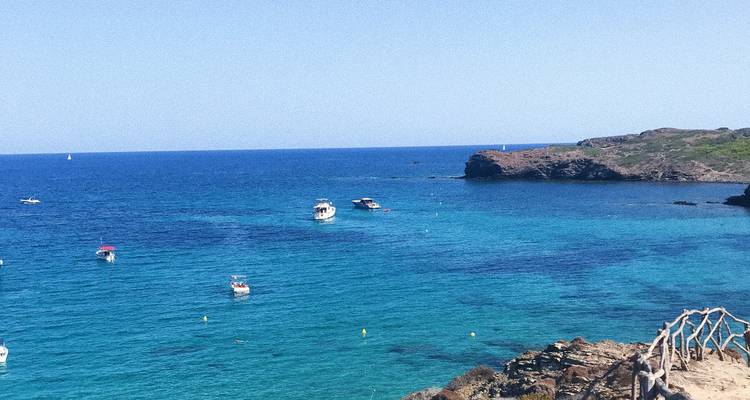 Mer turquoise avec des bateaux flottant près d'îles rocheuses.