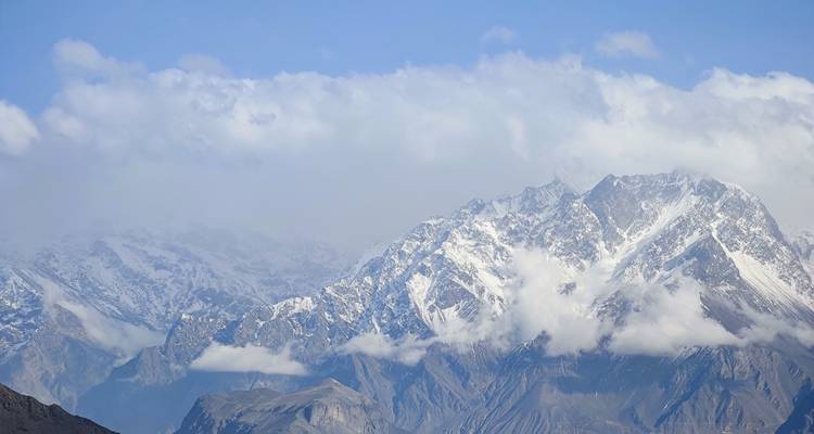 Picos montañosos dentados y cubiertos de nieve de la cordillera del Karakórum bajo un cielo azul con nubes dispersas.