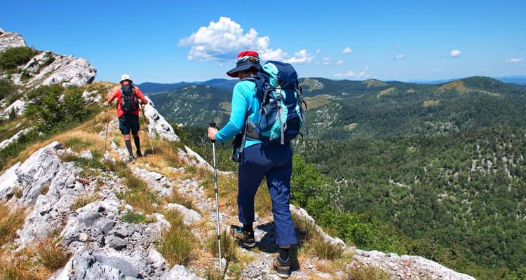 Hikers with backpacks on a rocky trail overlooking vast green hills.