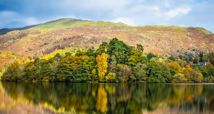 Vibrant autumn trees reflected in a calm lake with mountains.