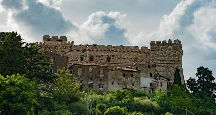 Mittelalterliche Festung auf einem Hügel, umgeben von Grün.
