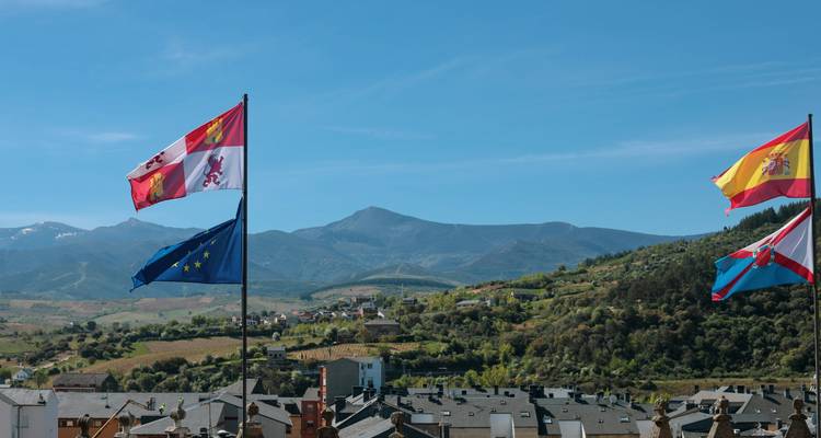 Fahnen, die über einer Stadtsilhouette mit Bergen im Hintergrund wehen.