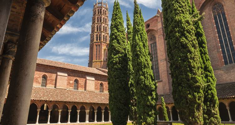 A view of a historic cloister with tall cypress trees and a brick church tower.