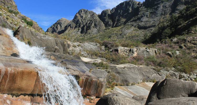 Waterfall cascading over rocks with mountains in the background.