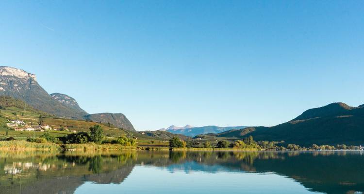 Lake with mountain backdrop, village buildings visible by the shore.