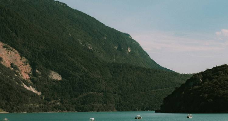 Lago sereno rodeado de montañas empinadas y boscosas bajo un cielo despejado.