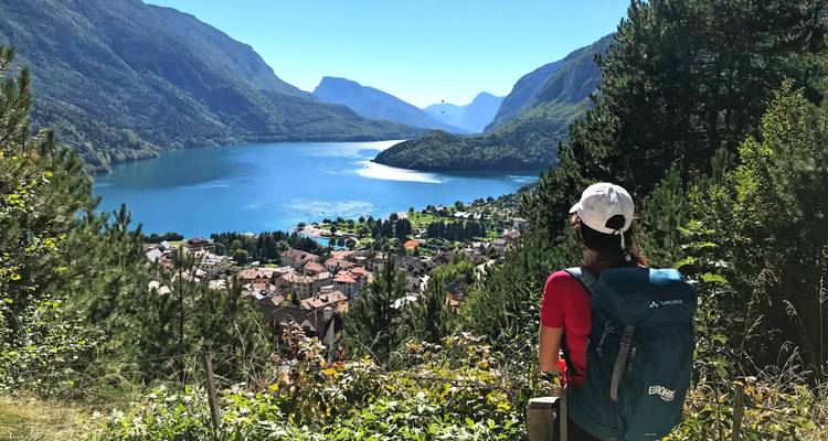 Solo hiker with backpack gazes over deep blue alpine lake surrounded by towering peaks.