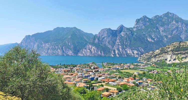 Panoramic view of an Italian lakeside town with turquoise water and steep alpine mountains under a clear blue sky