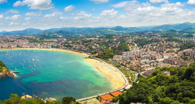 Panoramic beach and city view with mountains in the background.