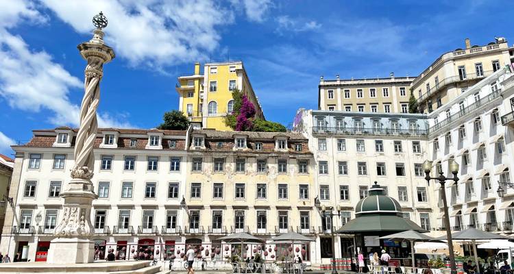 Place ensoleillée de Lisbonne avec bâtiments néoclassiques blancs, monument à colonne spiralée et bougainvilliers en fleurs.