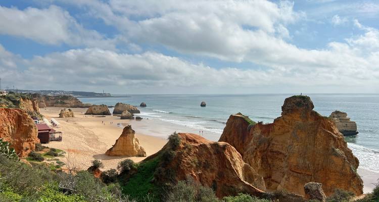Large plage de sable bordée de falaises dorées spectaculaires et d'eau turquoise de l'Atlantique sous un ciel partiellement nuageux.
