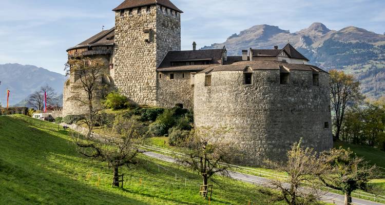 Château de pierre sur une colline verte avec des montagnes en arrière-plan.