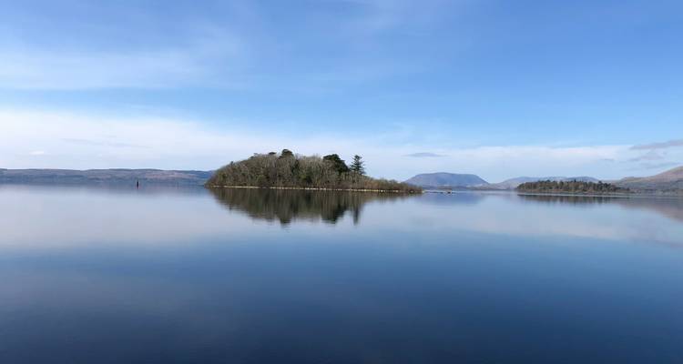 Serene lake with a small forested island, mountains in the distance.