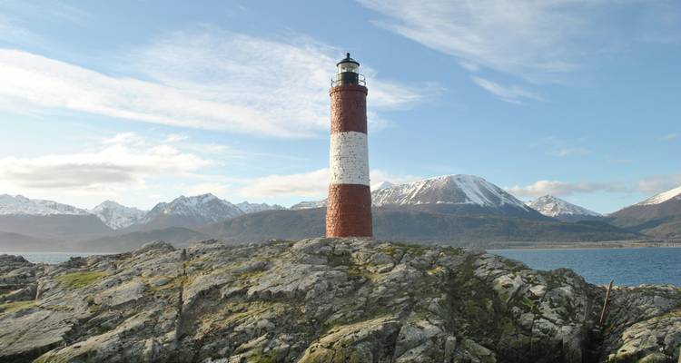 Lighthouse on a rocky island with mountains.