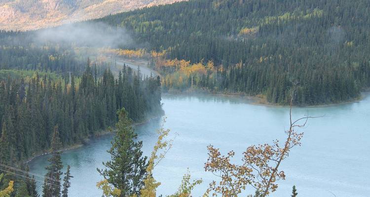 Lac serein entouré de forêt et de montagnes avec de la brume.