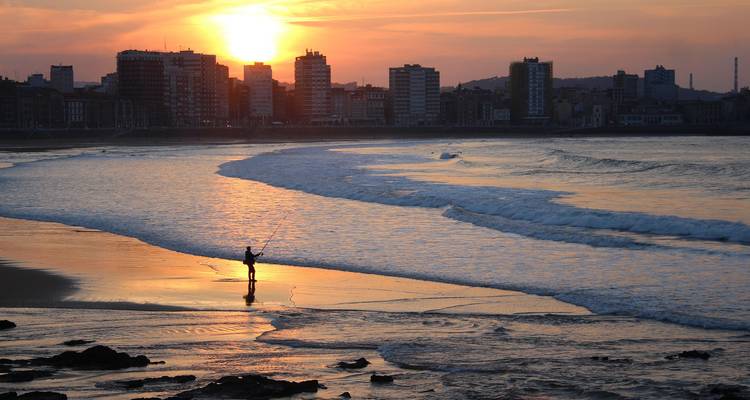 Coucher de soleil sur un horizon urbain avec une personne solitaire qui pêche au premier plan.