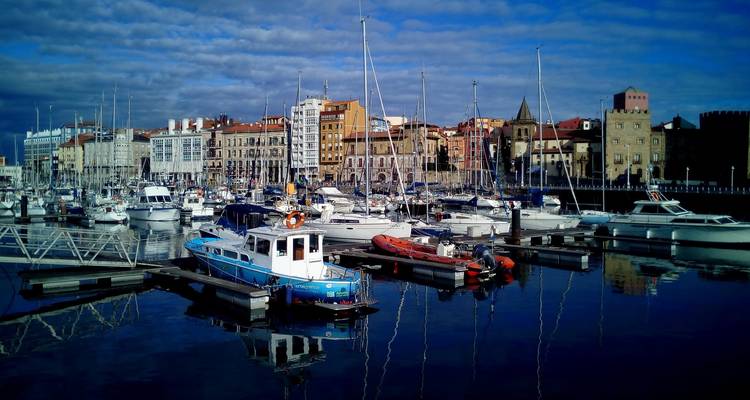 Scène de port avec des bateaux et des bâtiments historiques reflétés dans l'eau.