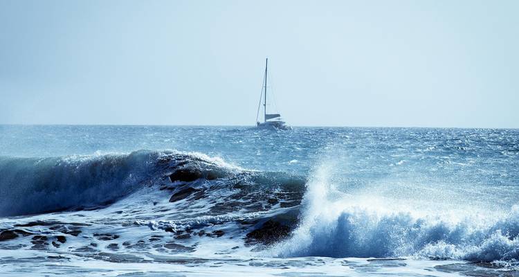 Voilier sur l'océan avec des vagues qui se brisent au premier plan.
