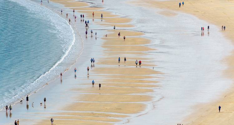 Des gens qui marchent le long du rivage sur une large plage de sable.
