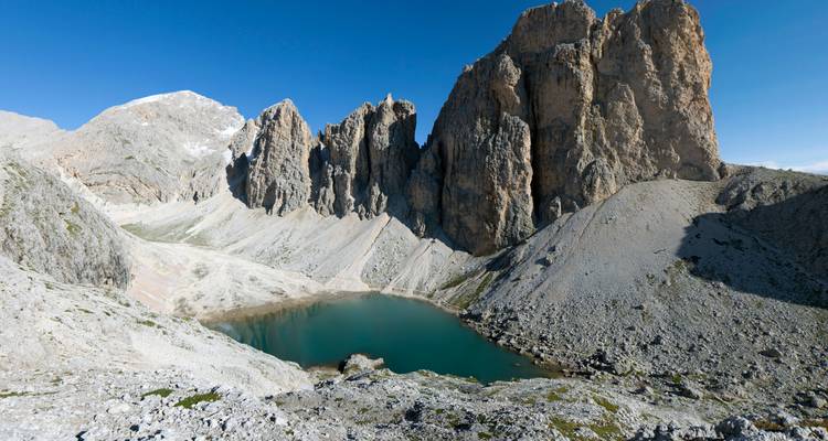 A rocky mountain range with a small lake at its base under a clear blue sky.