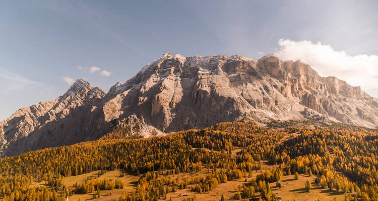 Una majestuosa cordillera montañosa con bosque otoñal en su base bajo cielos despejados.