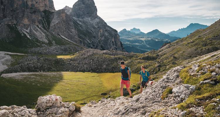 Excursionistas en un sendero rocoso en medio de un paisaje montañoso bajo un cielo despejado.