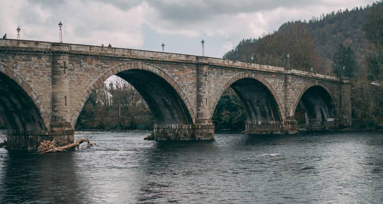 Stone arched bridge over a river with a cloudy backdrop.