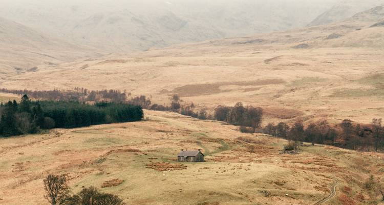 Remote cottage in a vast, hilly landscape under moody skies.