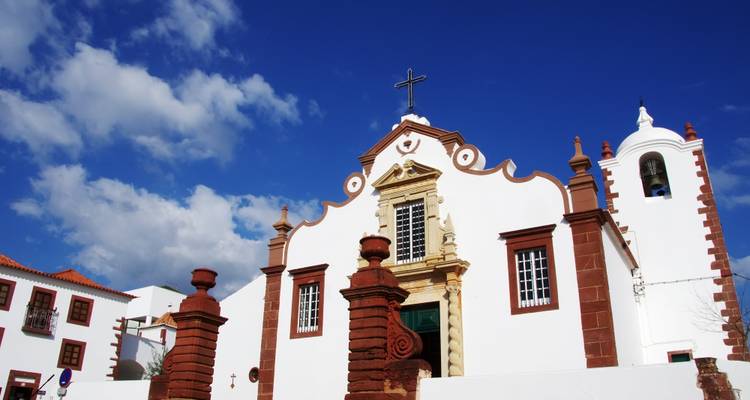 Église blanchie à la chaux avec des garnitures en grès rouge et un clocher qui se détache sur le ciel bleu profond de l'Algarve.