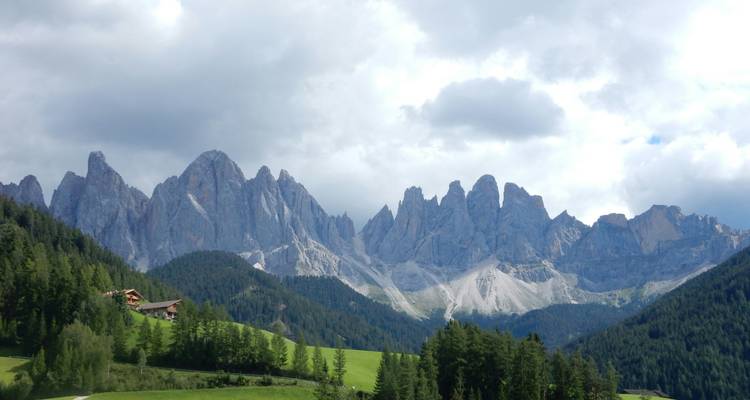 A lush valley with high rocky peaks under a cloudy sky.
