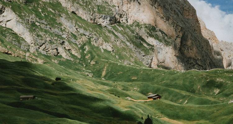 Green slopes with small wooden huts against a mountain backdrop.