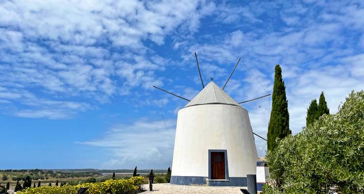 Eine traditionelle weiße Windmühle mit langen Flügeln steht auf einem Hügel unter einem Himmel mit flauschigen Wolken gesprenkelt.