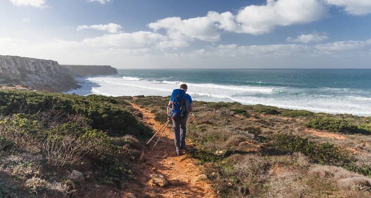 Person wandert entlang einer Küste mit Klippen und Meereswellen.