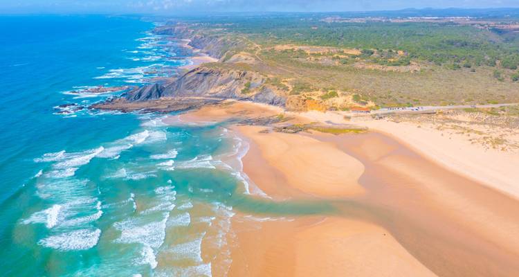 Drohnenaufnahme eines Küstengebiets mit Klippen und sanften Wellen.