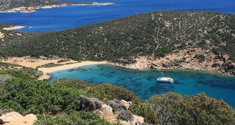 Blick auf eine Yacht in einer türkisfarbenen Bucht, umgeben von Hügeln.