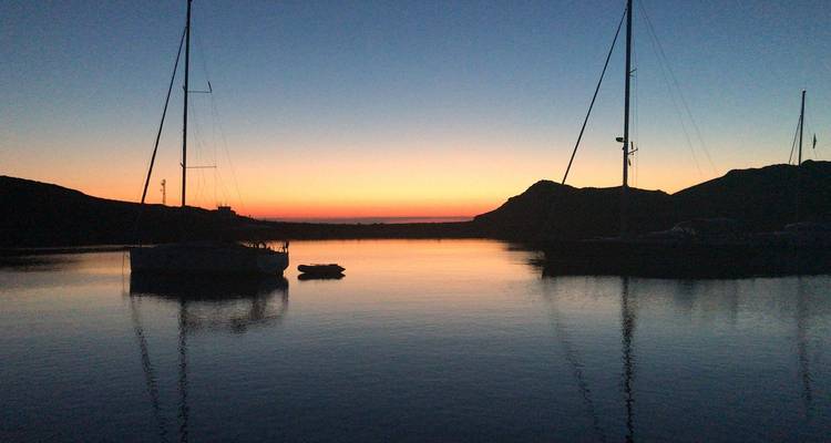 Silhouetten von Booten bei Sonnenuntergang in einem ruhigen Hafen.