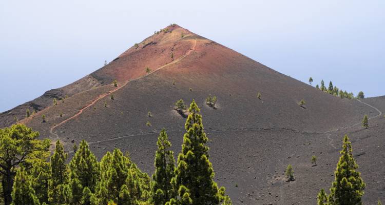 Colline volcanique conique avec végétation éparse et sentiers.